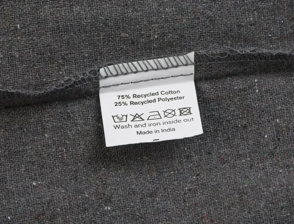 Label on dark grey fabric stating 75% recycled cotton, 25% recycled polyester and wash and iron inside out